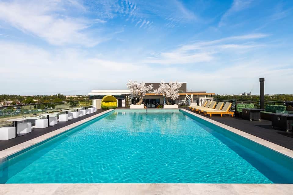 Resort rooftop pool with turquoise water, white lounge chairs, yellow loungers, and modern skyline backdrop