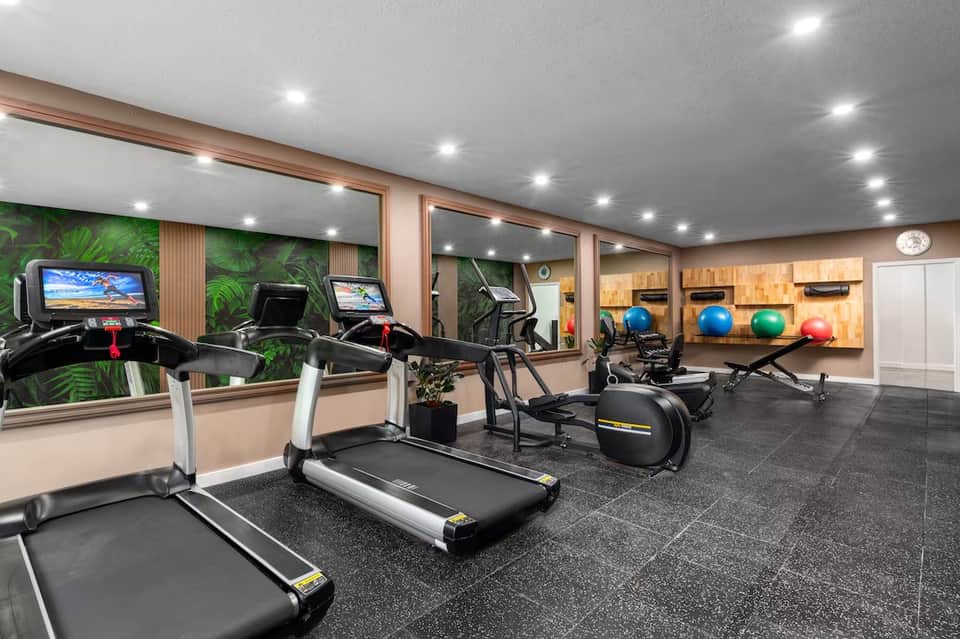 Modern fitness center with treadmills, exercise bikes, mirrors, and green accent wall