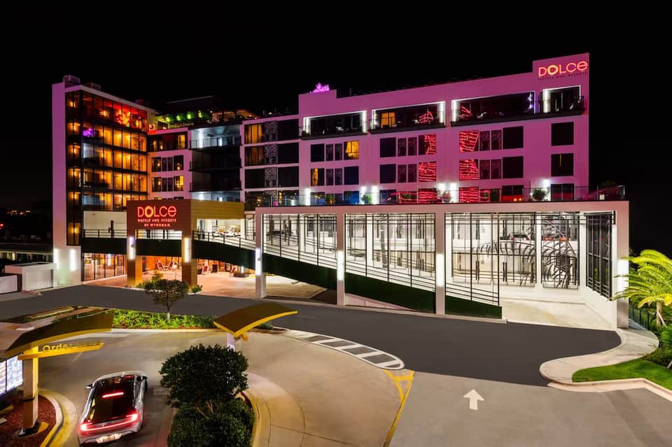 Modern pink and orange hotel building illuminated at night with parking area and entrance