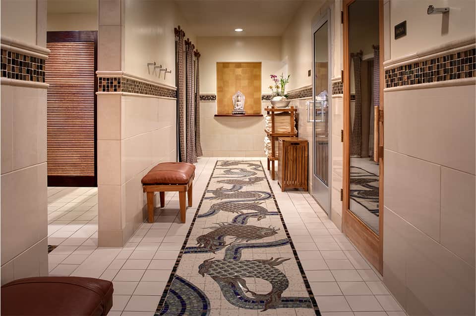 Spa corridor with decorative mosaic floor featuring fish patterns, tiled walls, and wooden accents