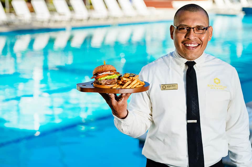 Server in white uniform holding plate with burger and fries by indoor swimming pool
