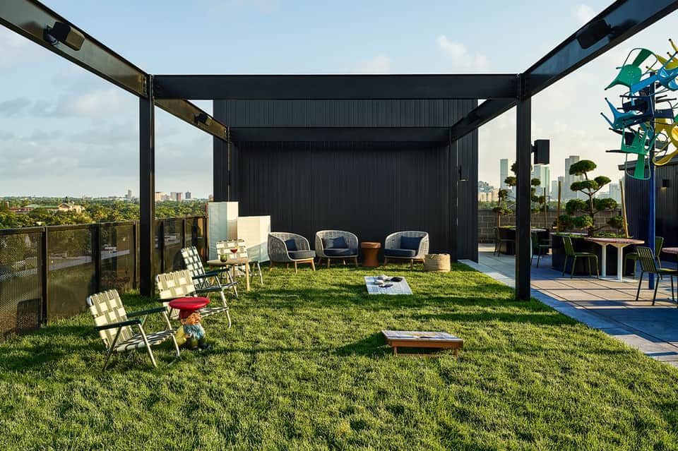 Rooftop terrace with black pergola, grass lawn, blue chairs, and city skyline view