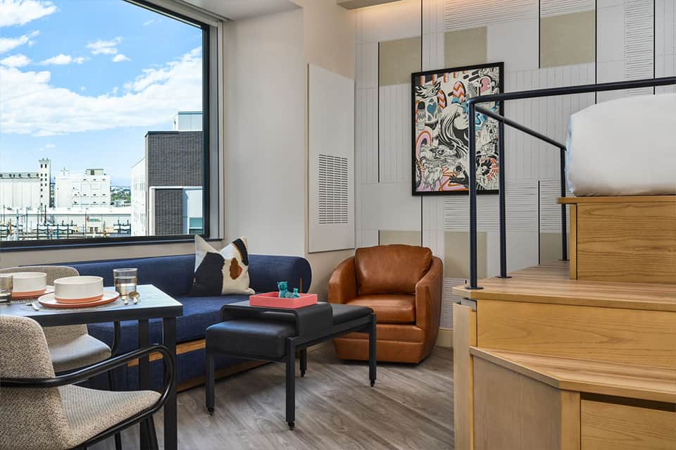 Modern hotel room with blue sofa, city views, and contemporary furnishings