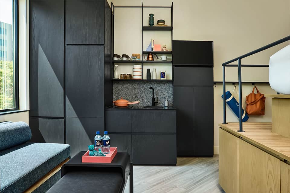 Contemporary hotel suite with black cabinetry, kitchenette, gray upholstered seating, and open layout design