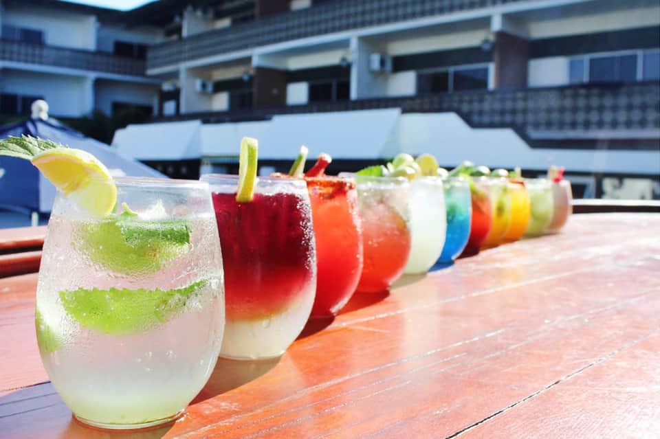 Colorful cocktails lined up on a wooden deck with a resort building in the background