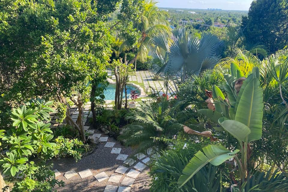 Elevated view of tropical gardens with winding stone pathway, palm trees, lush vegetation, and pool visible in background