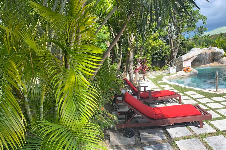 Red lounge chair nestled under palm trees overlooking a tropical lagoon pool