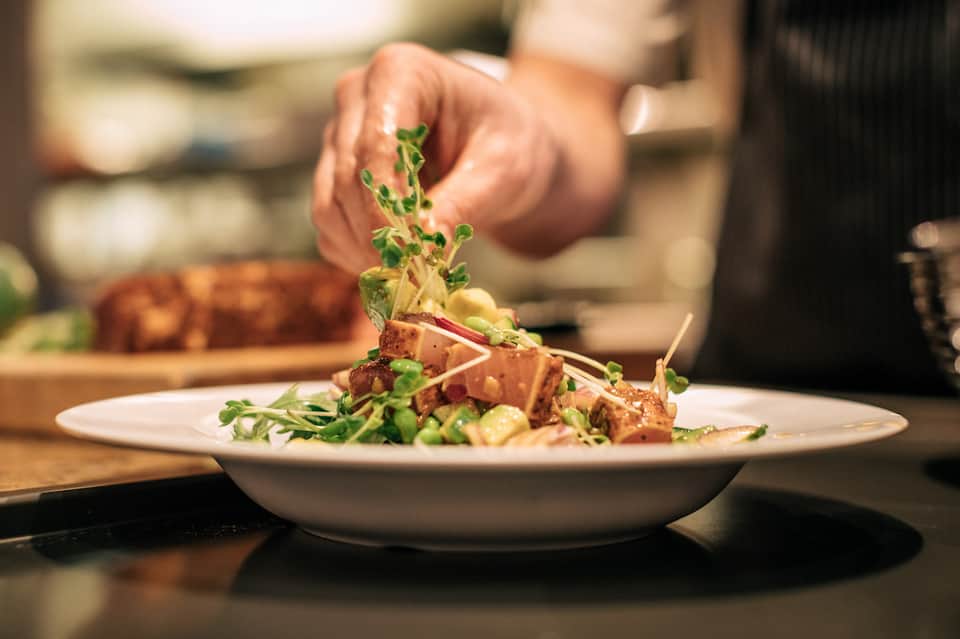 Chef plating gourmet dish with microgreens at fine dining restaurant