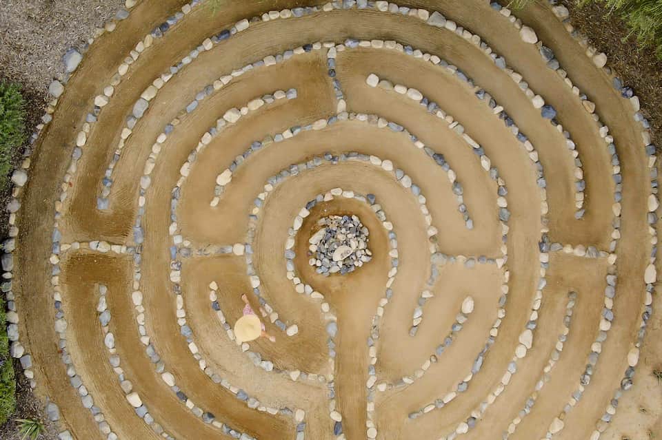 Aerial view of decorative spiral labyrinth pattern made with white and gray stones on brown earth