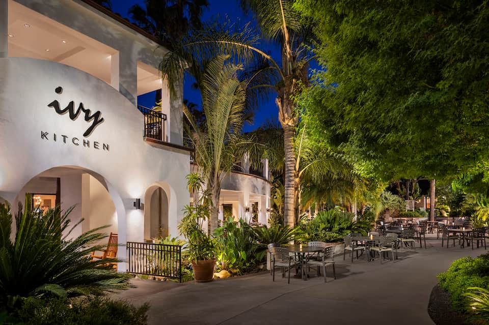 Ivy Kitchen restaurant exterior at night with white arches, palm trees, and outdoor seating