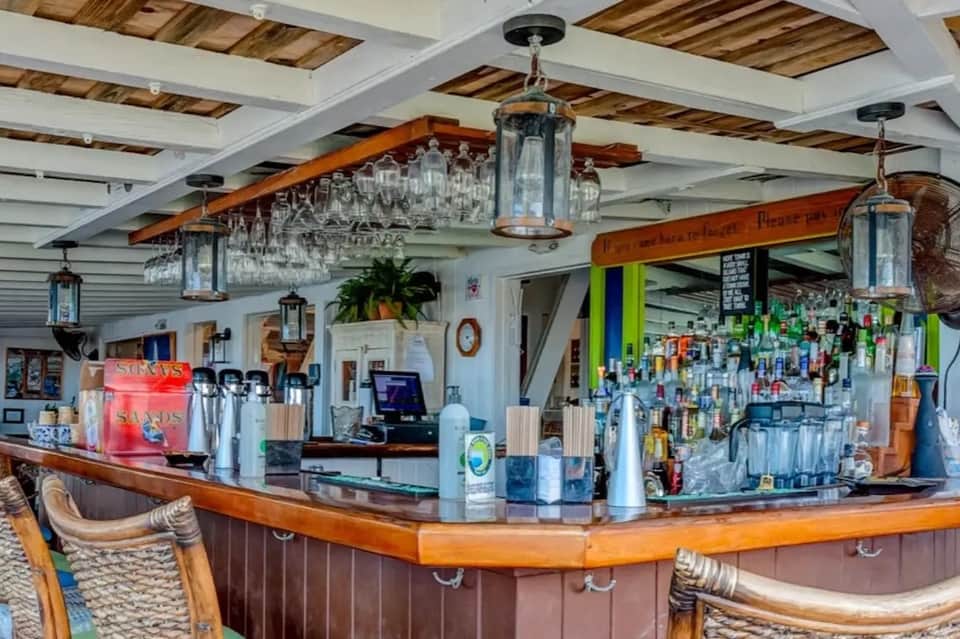 Rustic wooden bar counter with hanging glassware, colorful bottles, and nautical-themed décor