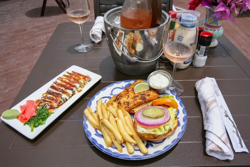 Outdoor dining table with sushi, grilled fish, fries, and beverages on dark surface