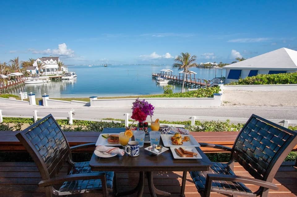 Waterfront dining table set for two overlooking calm blue bay with boats and white buildings