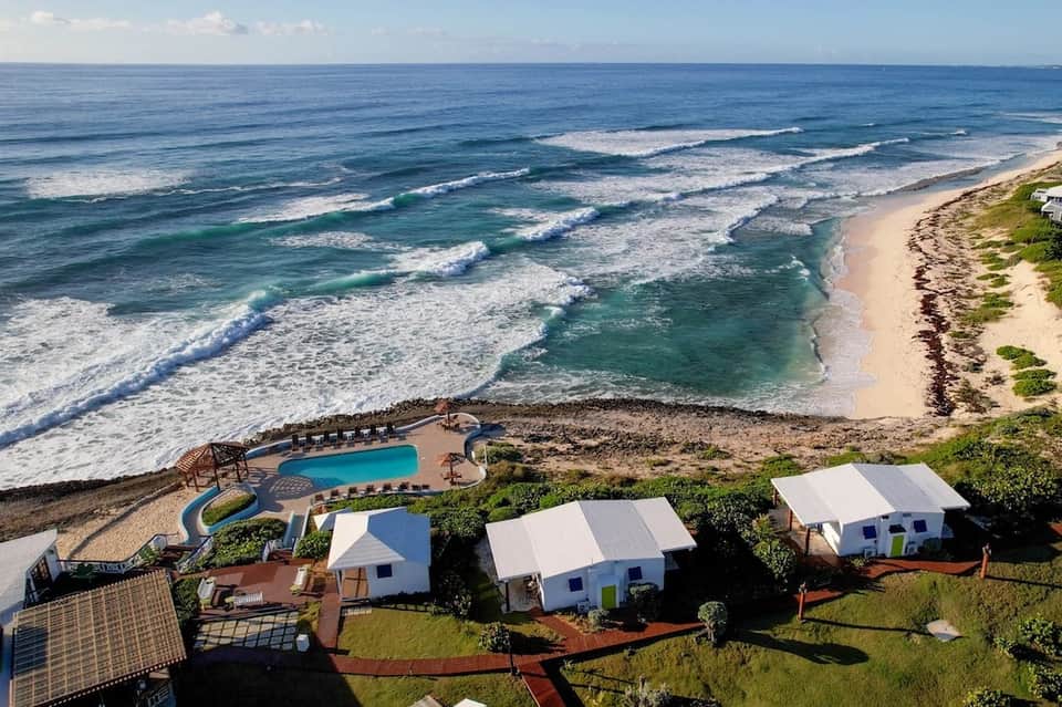 Aerial view of beachfront resort with white cabanas, pool, and ocean waves
