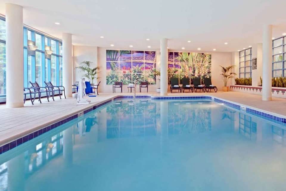 Indoor pool facility with blue water, columns, large windows, and lounge seating areas