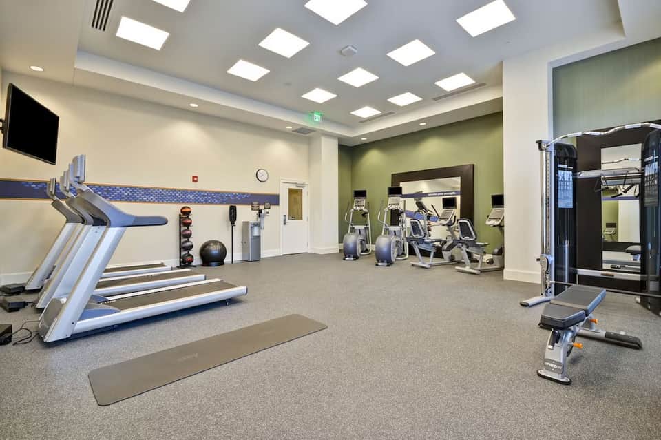 Modern fitness center with treadmills, exercise bikes, and equipment on gray carpet flooring