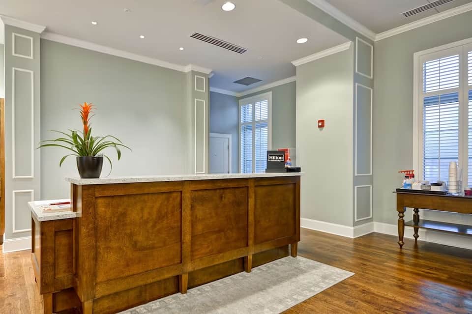 Hotel lobby with wooden reception desk, potted plant, and pale green walls