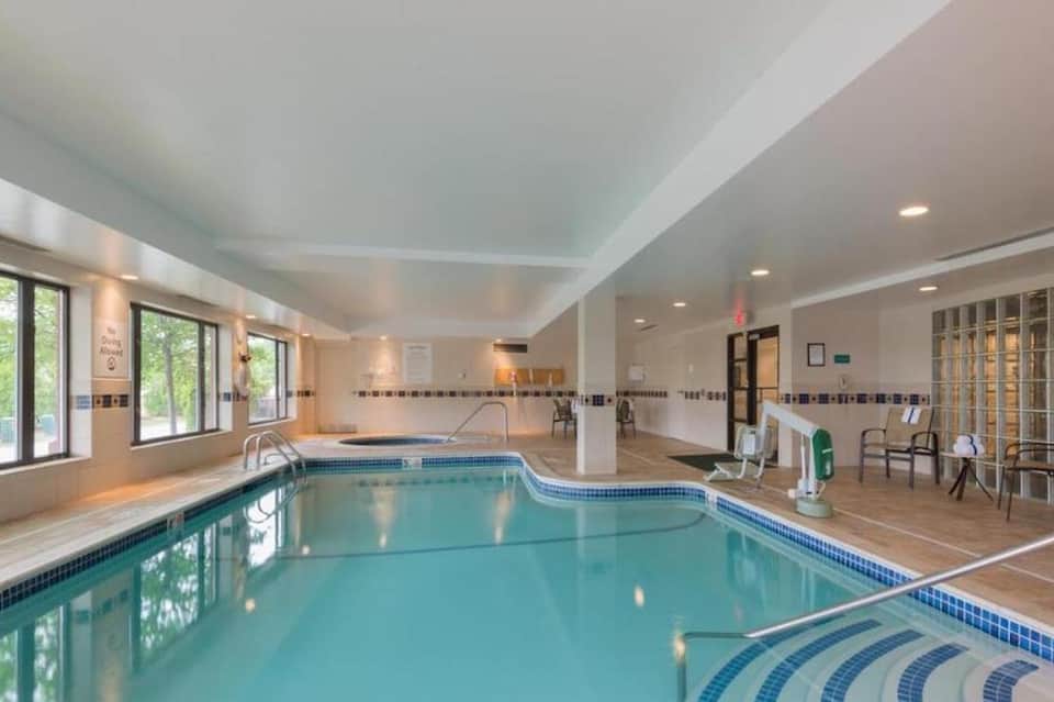 Indoor heated pool with curved design, blue tile accents, large windows, and adjacent spa area
