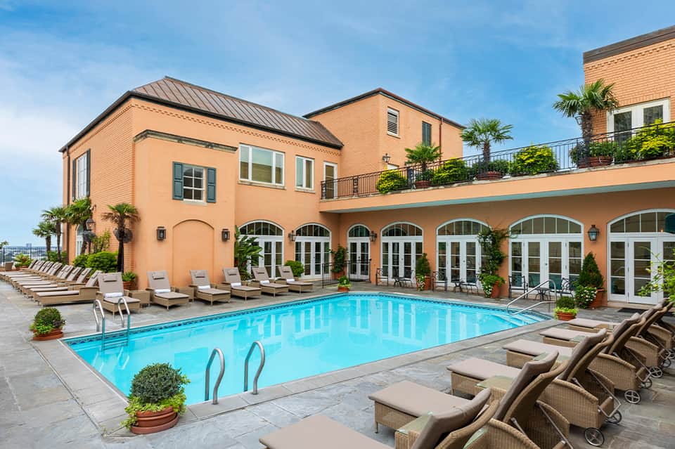 Elegant resort pool with tan loungers, peach-colored building facade with arched windows and lush landscaping