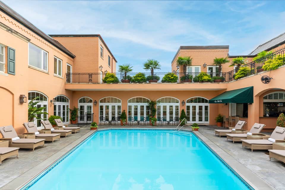 Indoor rectangular pool with cream loungers, arched columns, and terracotta building facade reflected in calm water