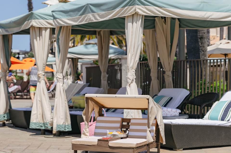 Resort poolside cabanas with cream-colored curtains and lounge seating