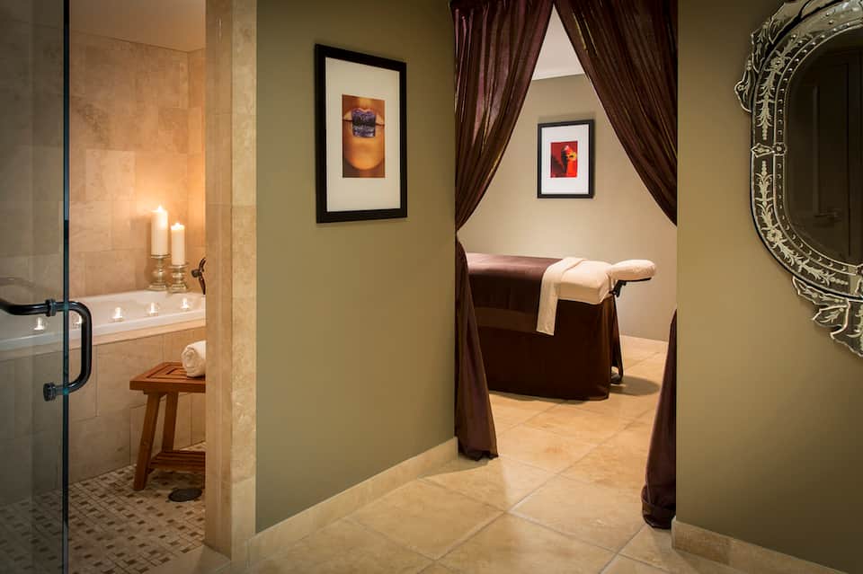 Spa bathroom with soaking tub, candles, and curtained relaxation area