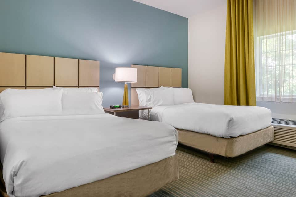 Hotel guest room with two queen beds, teal accent wall, and olive curtains