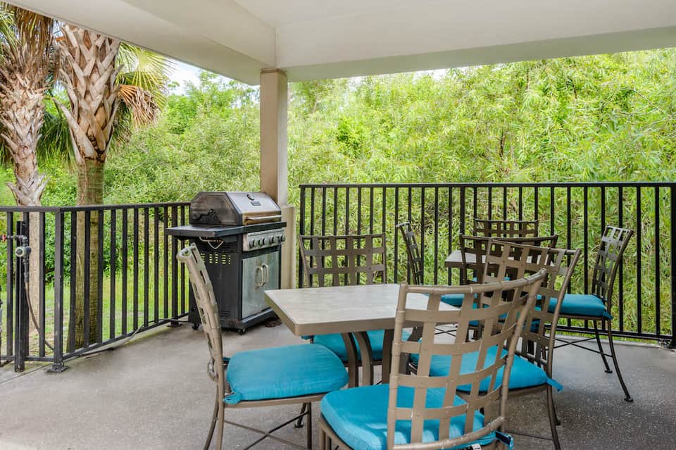 Covered patio with outdoor dining table, gas grill, and chairs overlooking lush green landscape