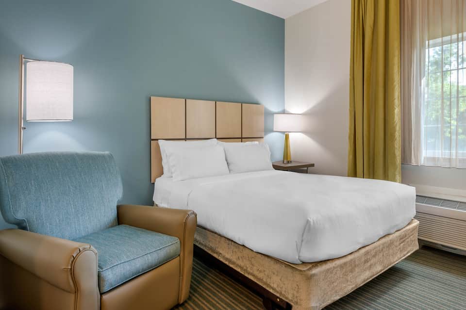 Modern hotel bedroom with queen bed, teal accent wall, and comfortable seating area