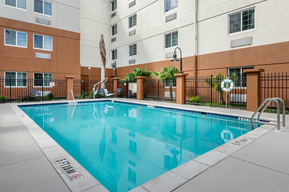 Indoor hotel swimming pool surrounded by brown walls, black fence, and manicured landscaping