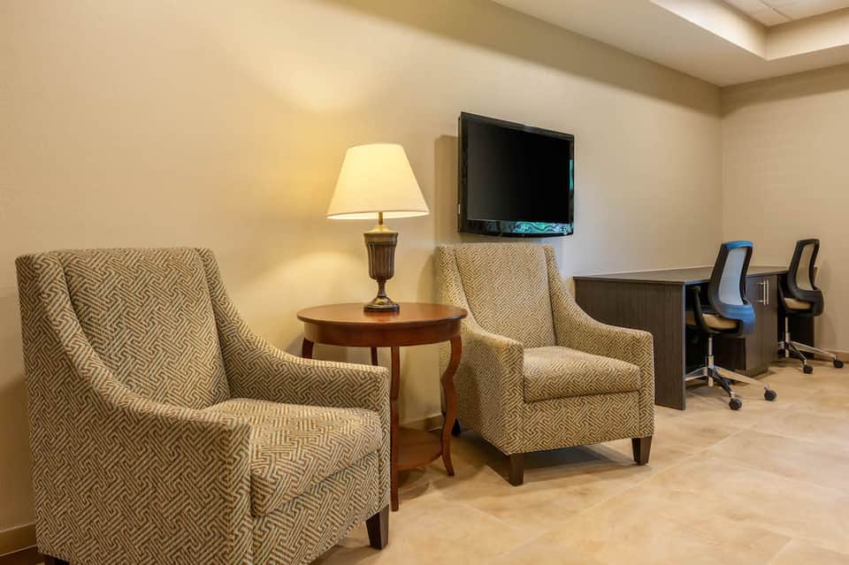 Modern hotel lounge with beige patterned armchairs, wooden table, lamp, and business desk area