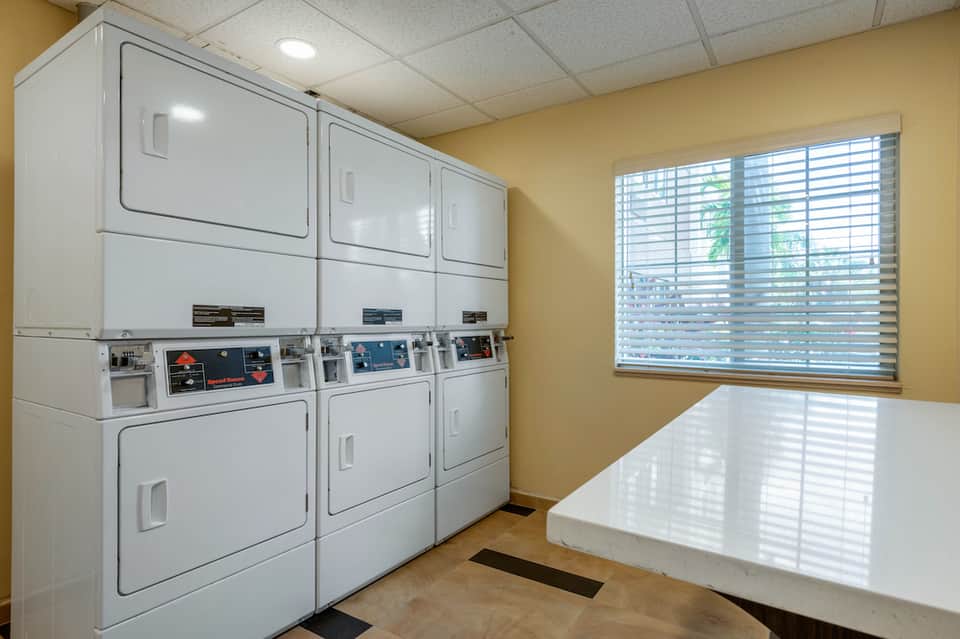 Laundry room with multiple white commercial dryers and folding table with yellow walls