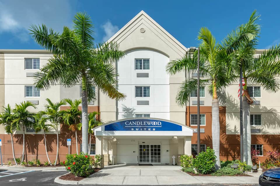 Candlewood Suites hotel exterior with white and orange facade, palm trees, and blue awning entrance