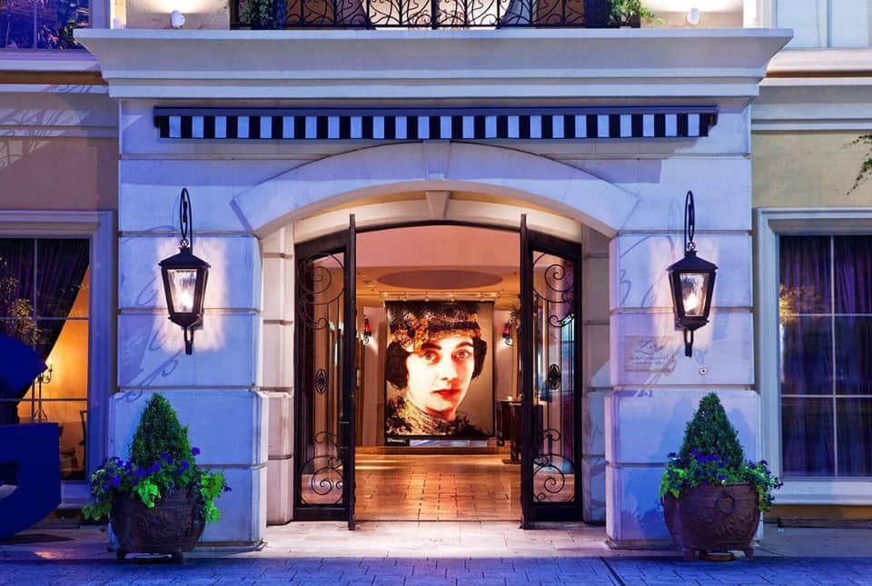 Illuminated hotel entrance with arched doorway, decorative ironwork, potted plants, and wall sconces at dusk