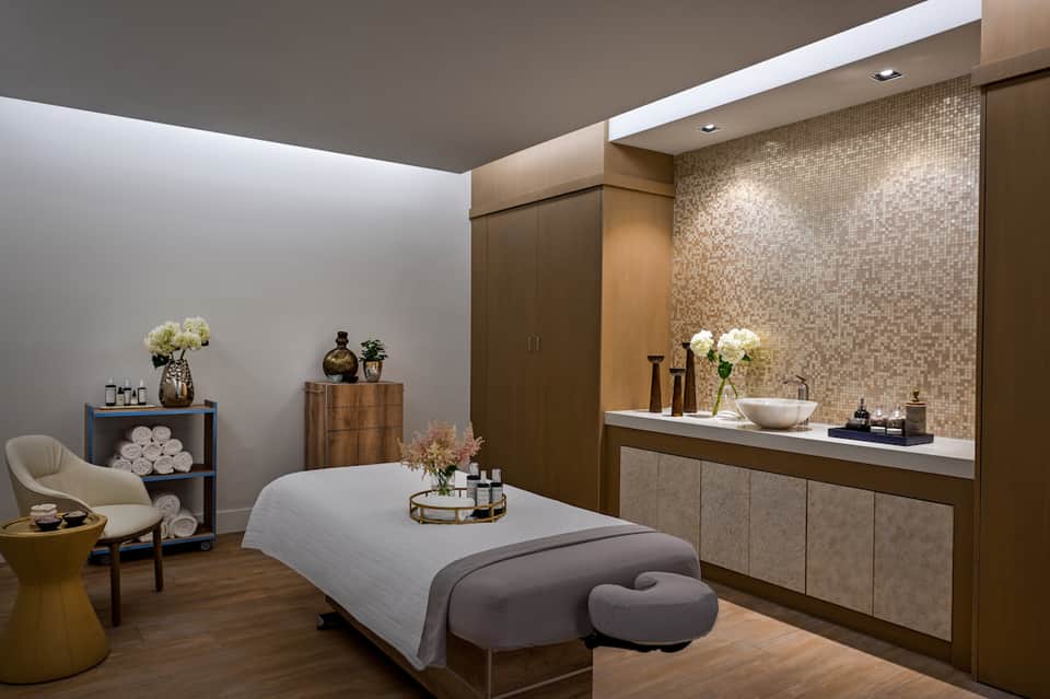 Modern spa treatment room with massage bed, neutral tones, and mosaic tile accents