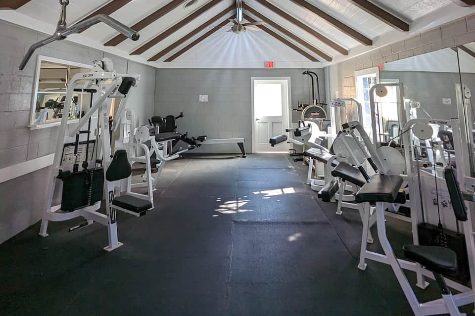 Spacious gym with white exercise machines, treadmills, and equipment under vaulted ceiling with skylights