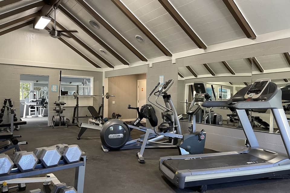 Bright fitness center with exposed beam ceiling, treadmills, exercise bikes, weight racks, and mirrors