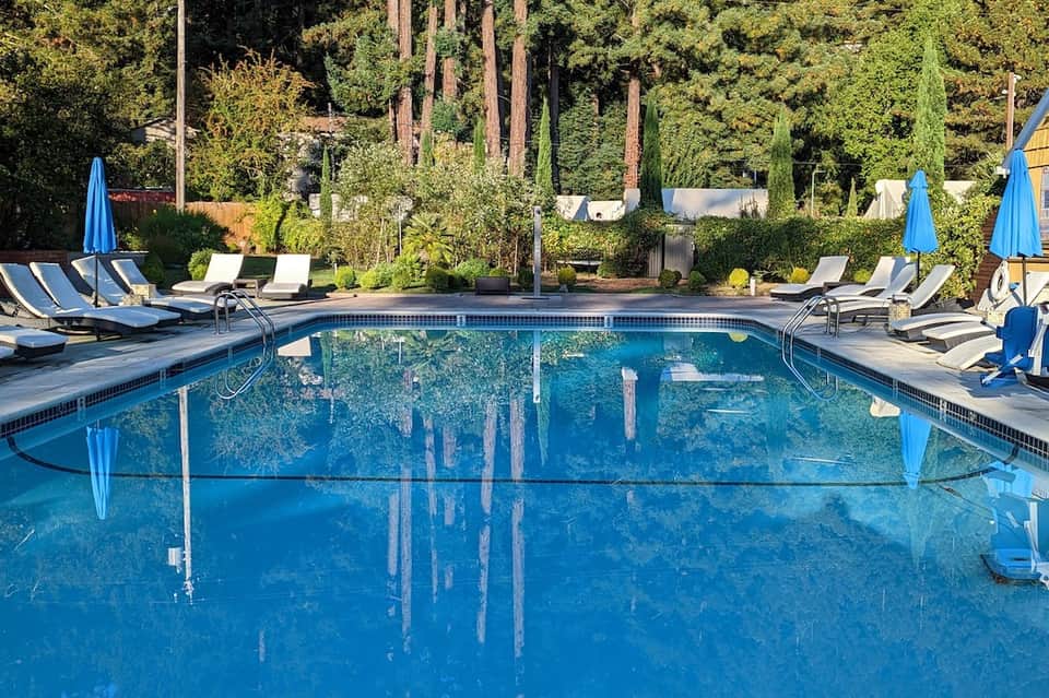Luxury pool surrounded by tall trees, blue umbrellas, and lounge seating area
