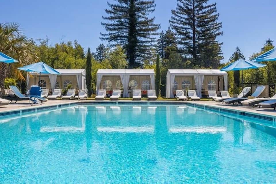 Resort outdoor swimming pool with turquoise water, white cabanas, loungers, and tall pine trees