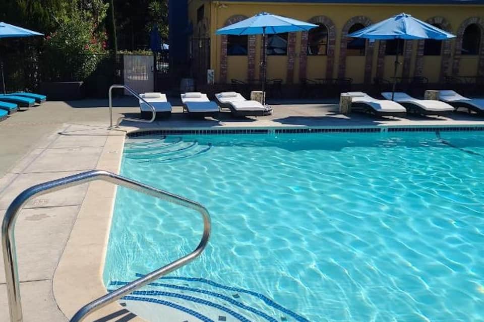 Resort pool with blue umbrellas, lounge chairs, and yellow building with arches