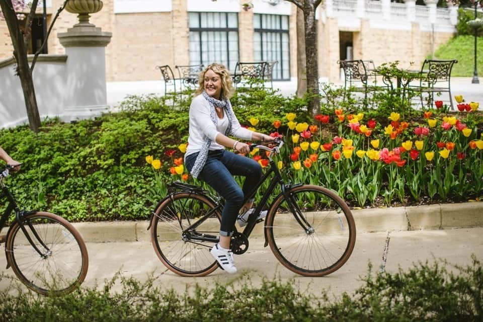Woman on vintage bicycle in courtyard garden with vibrant red and yellow tulips and manicured hedges