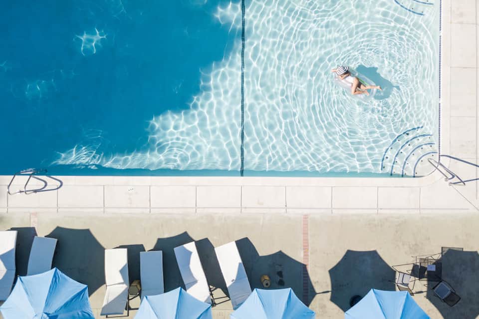 Overhead view of swimmer in lap pool with striped umbrellas poolside