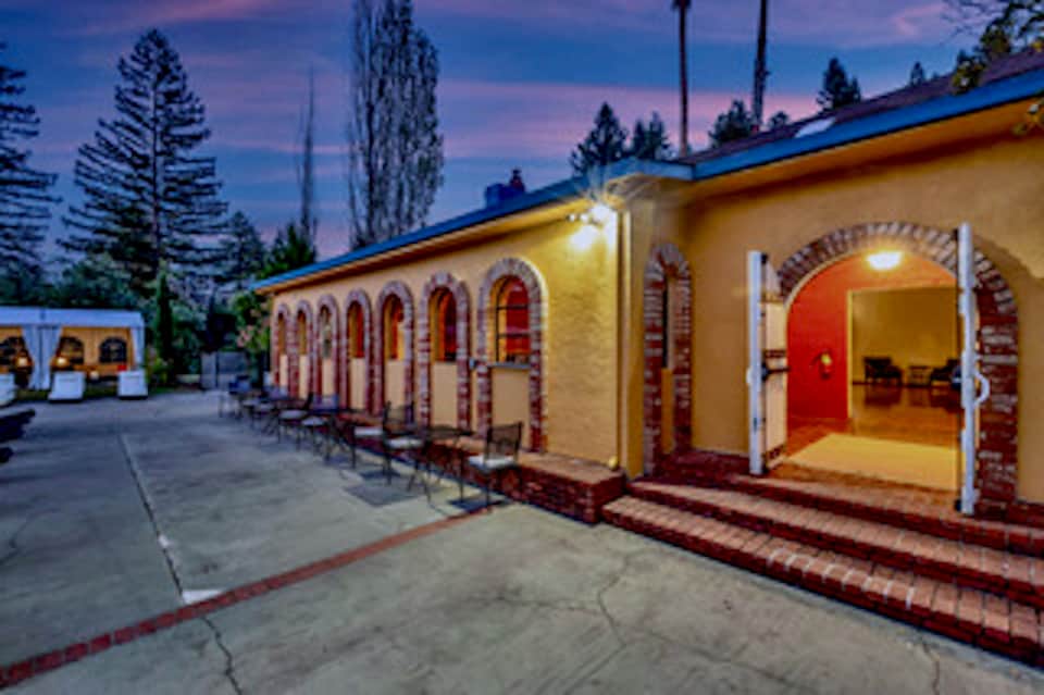 Row of illuminated cottage-style buildings with arched doorways at dusk surrounded by pine trees