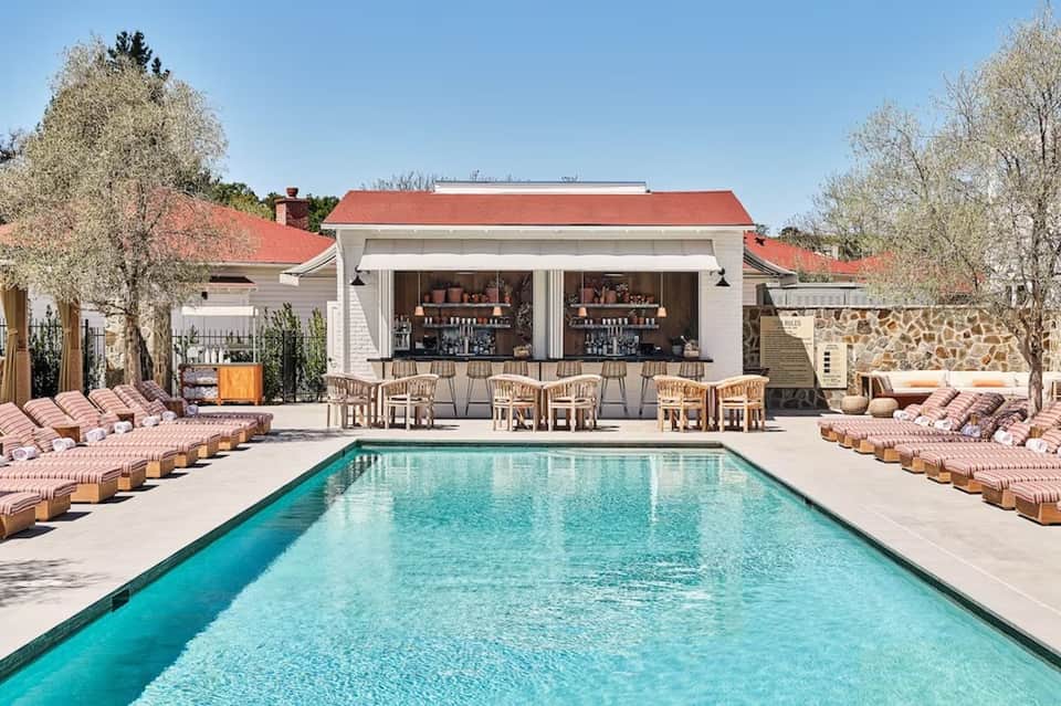 Resort pool with turquoise water, white clubhouse with red roof, lounge chairs, and blooming trees
