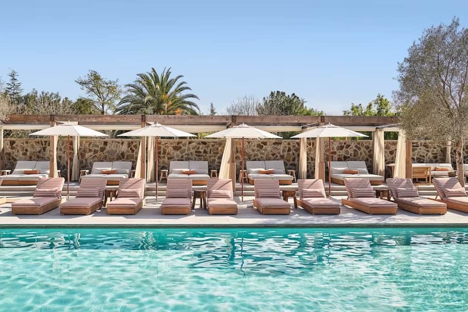 Resort pool with pink loungers and white umbrellas lined up alongside crystal-clear water