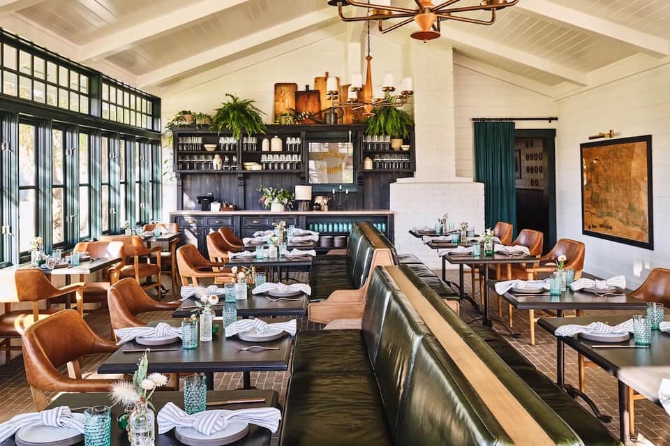 Upscale restaurant dining room with brown leather chairs, dark wood tables, and black bar backdrop