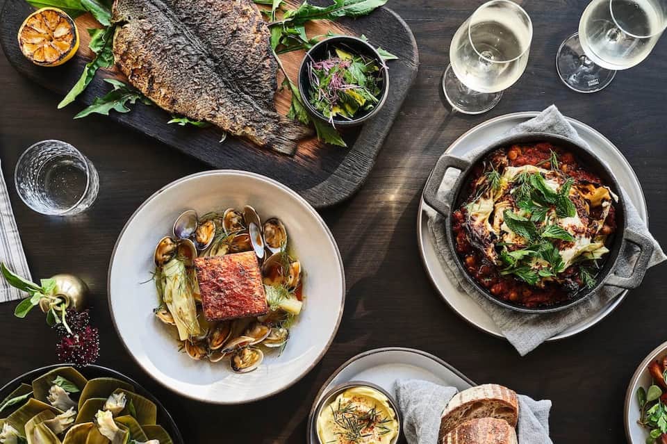 Fine dining table setting with grilled fish, seafood dishes, fresh salad, and wine glasses on dark wood