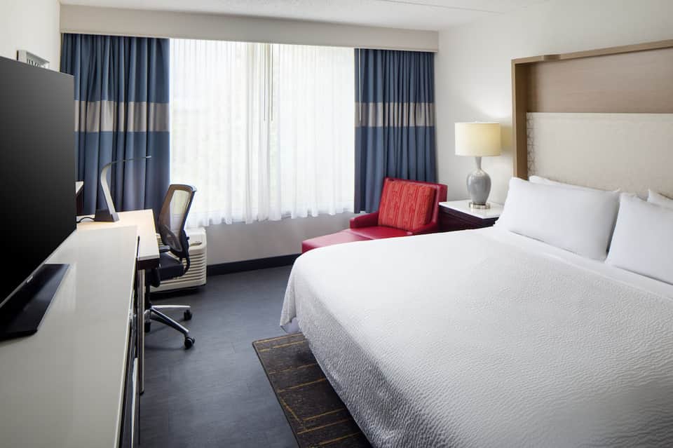 Modern hotel bedroom with king bed, work desk, blue striped curtains, and city view windows