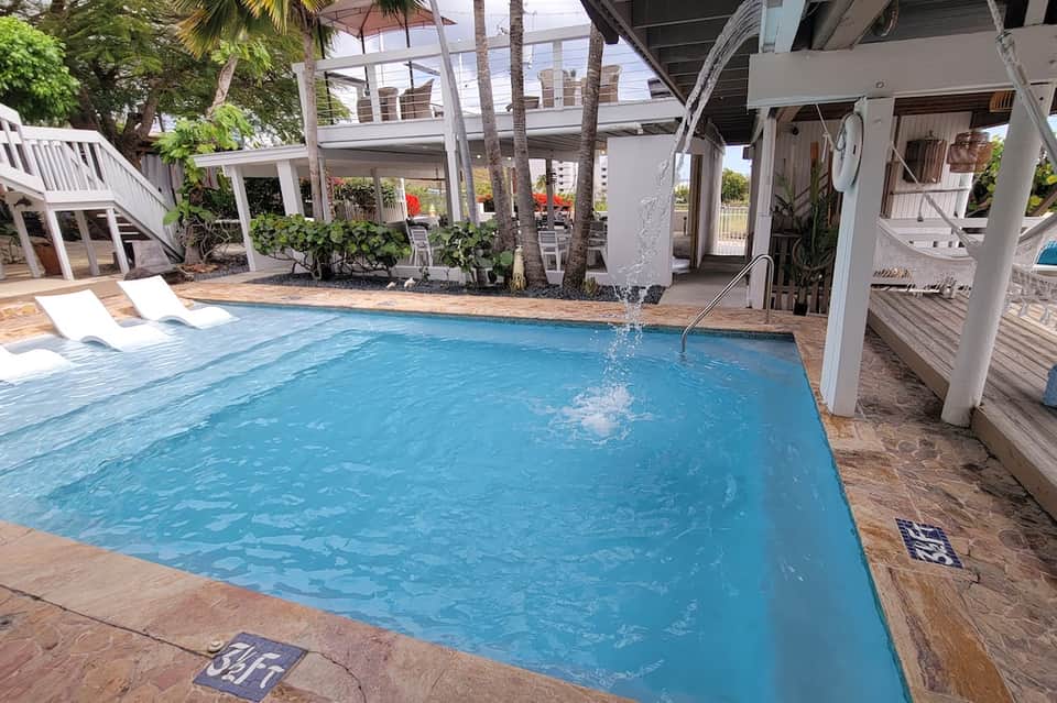 Rectangular swimming pool with lounge chairs and covered structures in a tropical resort setting