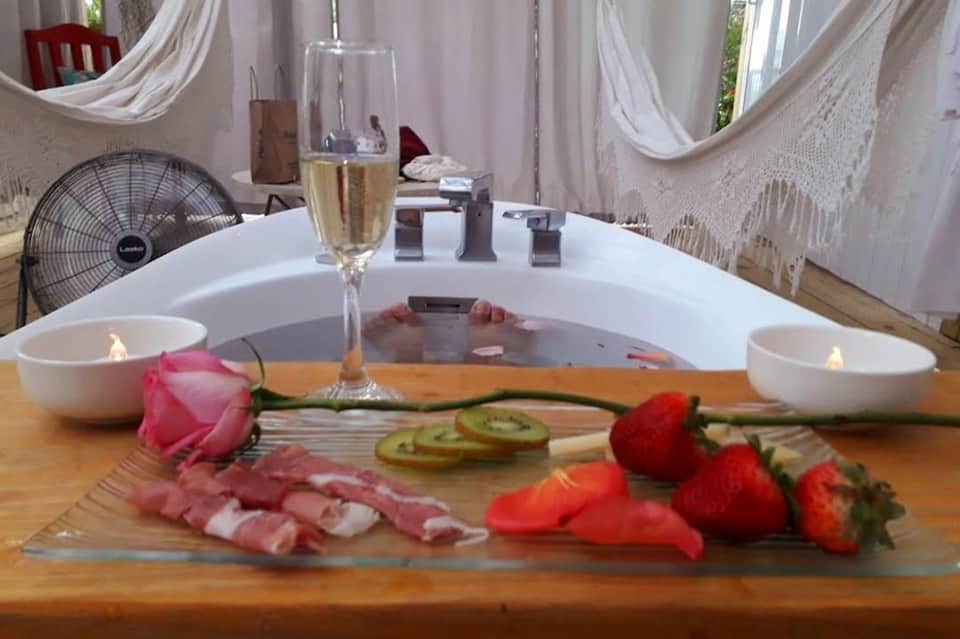 Romantic bath setup with champagne, strawberries, rose petals, and flowing white curtains